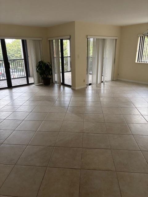 empty room with light tile patterned floors, a wealth of natural light, and baseboards