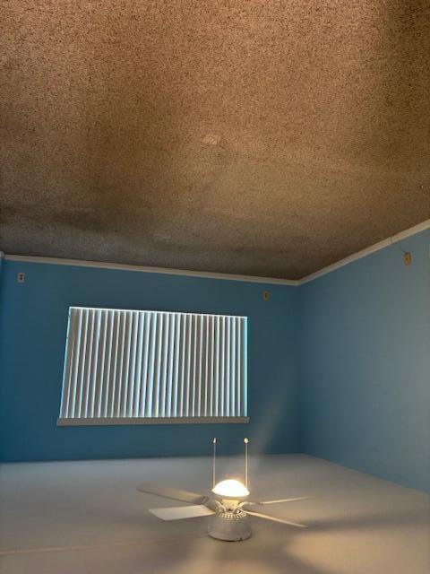 empty room featuring a ceiling fan, crown molding, and a textured ceiling