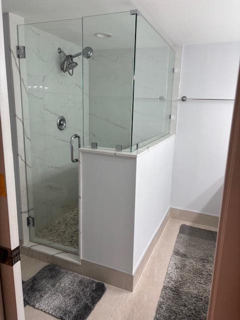 bathroom featuring tile patterned flooring, a marble finish shower, and baseboards