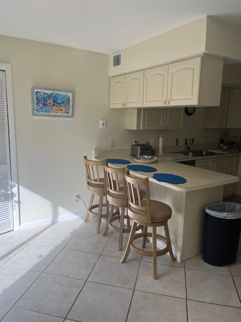 kitchen featuring light tile patterned floors, a breakfast bar area, a peninsula, a sink, and light countertops