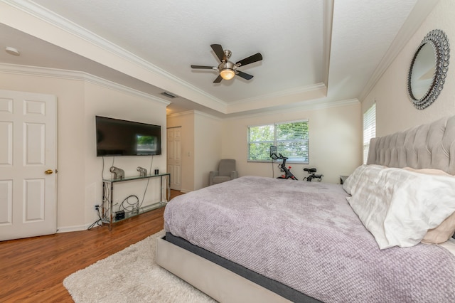 bedroom with hardwood / wood-style flooring, ceiling fan, ornamental molding, and a tray ceiling