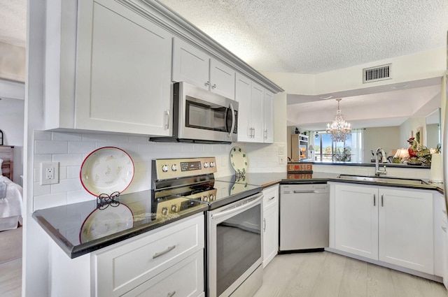 kitchen with light wood-type flooring, a textured ceiling, sink, an inviting chandelier, and stainless steel appliances