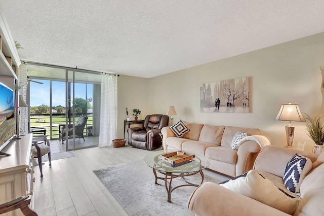 living room featuring light wood-type flooring, a textured ceiling, and a wall of windows