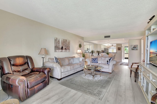 living room featuring a notable chandelier, light wood-type flooring, and a textured ceiling