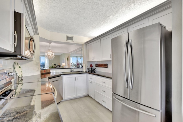 kitchen with sink, backsplash, appliances with stainless steel finishes, dark stone counters, and light hardwood / wood-style floors