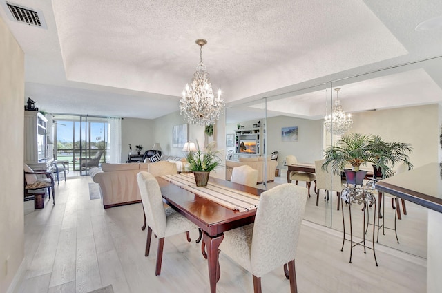 dining space featuring light hardwood / wood-style floors, a textured ceiling, a notable chandelier, a raised ceiling, and a wall of windows