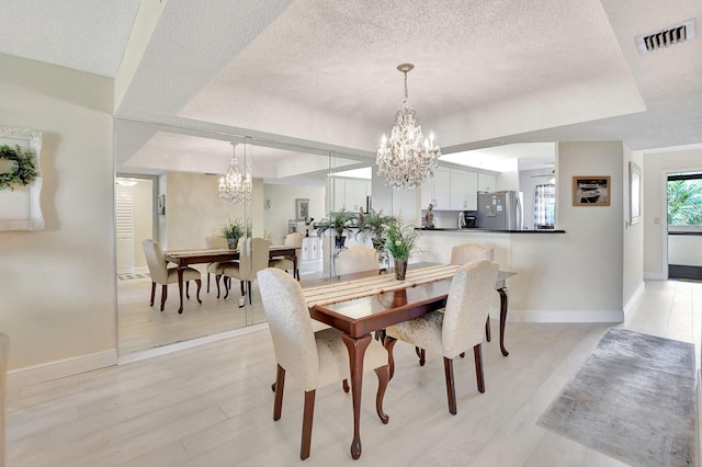 dining area featuring a textured ceiling, light wood-type flooring, and a tray ceiling