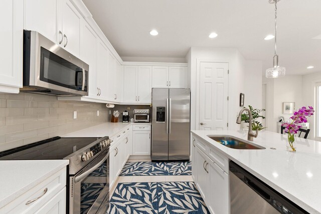 kitchen featuring white cabinetry, sink, hanging light fixtures, stainless steel appliances, and a kitchen island with sink