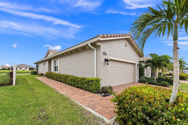 view of home's exterior featuring driveway, stucco siding, a garage, a tiled roof, and a lawn