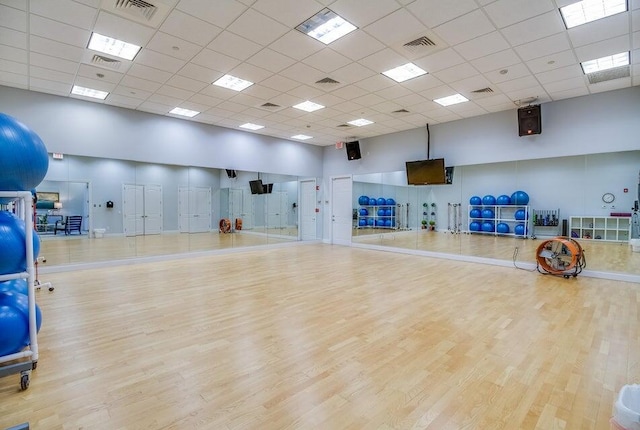 workout area featuring a paneled ceiling, light wood-type flooring, and a towering ceiling