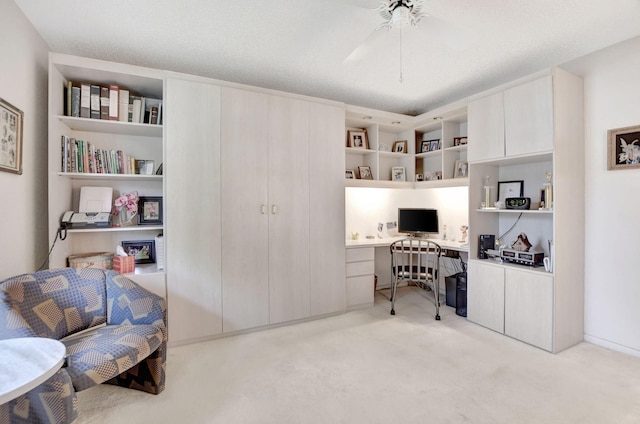 carpeted office featuring built in desk, a textured ceiling, and ceiling fan