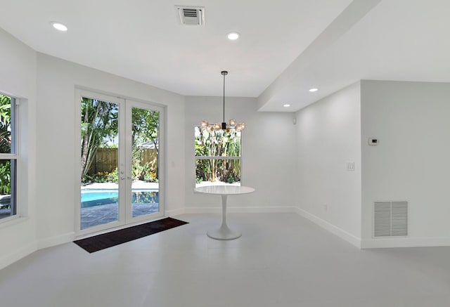 unfurnished dining area with concrete flooring, an inviting chandelier, and french doors