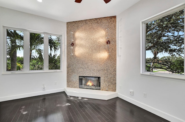 unfurnished living room with a wealth of natural light, a large fireplace, hardwood / wood-style flooring, and ceiling fan