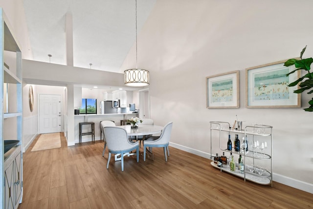 dining space with high vaulted ceiling and light wood-type flooring