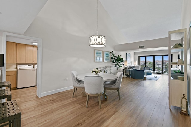 dining area featuring washer / clothes dryer, high vaulted ceiling, and light hardwood / wood-style floors