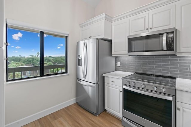 kitchen with light hardwood / wood-style flooring, appliances with stainless steel finishes, tasteful backsplash, light stone counters, and white cabinetry