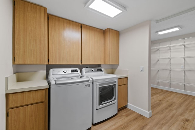 washroom featuring washing machine and dryer, light hardwood / wood-style flooring, and cabinets