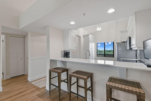 kitchen with a kitchen breakfast bar, backsplash, kitchen peninsula, white cabinets, and appliances with stainless steel finishes