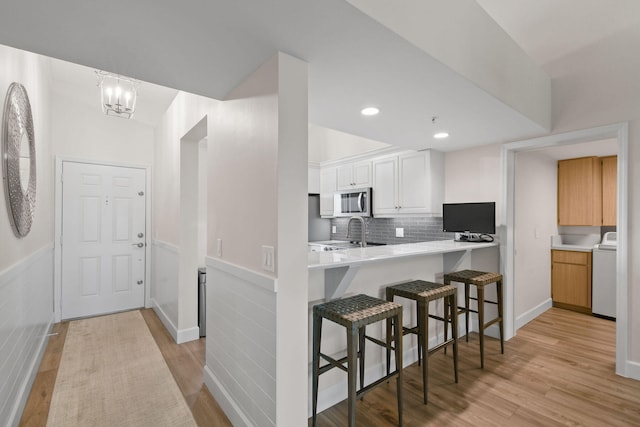 kitchen with a breakfast bar, light hardwood / wood-style flooring, decorative backsplash, white cabinetry, and washer / clothes dryer