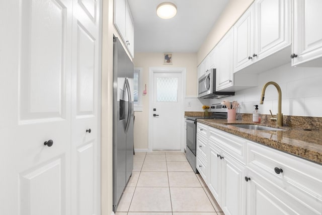 kitchen with light tile patterned floors, sink, white cabinetry, stainless steel appliances, and dark stone countertops