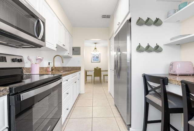 kitchen with appliances with stainless steel finishes, dark stone countertops, white cabinets, light tile patterned floors, and sink