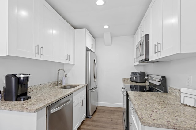 kitchen with appliances with stainless steel finishes, light hardwood / wood-style floors, light stone counters, white cabinets, and sink