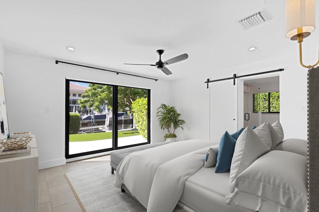 tiled bedroom featuring multiple windows, ceiling fan, and a barn door