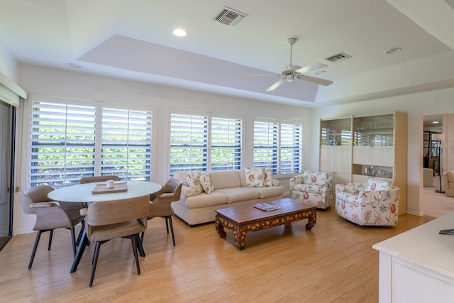 living room featuring ceiling fan, light hardwood / wood-style flooring, and a tray ceiling