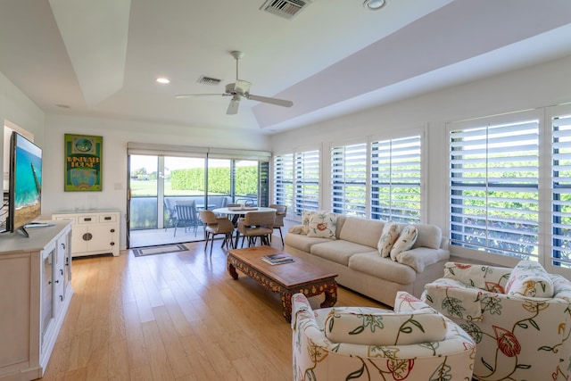 living room with light hardwood / wood-style floors, a raised ceiling, a wealth of natural light, and ceiling fan