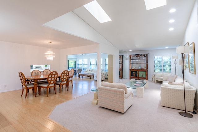 living room with an inviting chandelier, light hardwood / wood-style floors, lofted ceiling with skylight, and plenty of natural light