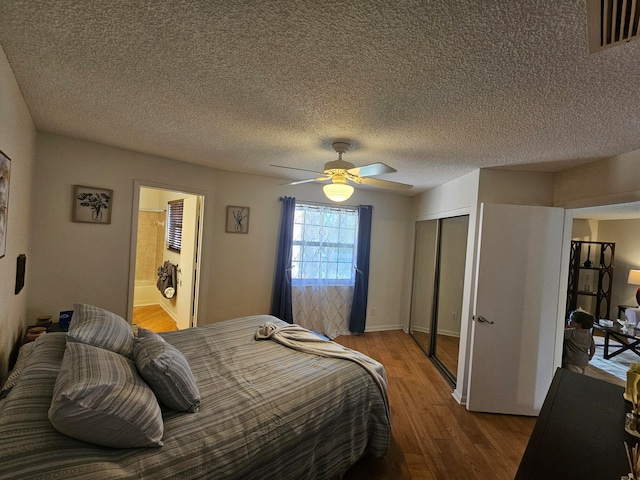 bedroom featuring ceiling fan, wood-type flooring, a textured ceiling, a closet, and ensuite bath