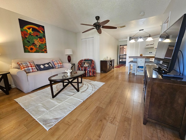 living room with light hardwood / wood-style flooring, ceiling fan, and a textured ceiling