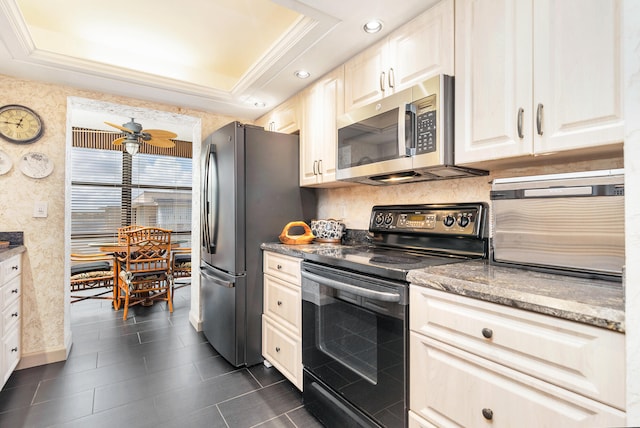 kitchen featuring dark tile patterned flooring, a raised ceiling, appliances with stainless steel finishes, dark stone countertops, and ceiling fan