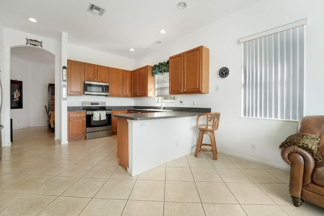 kitchen with sink, appliances with stainless steel finishes, kitchen peninsula, and light tile patterned floors