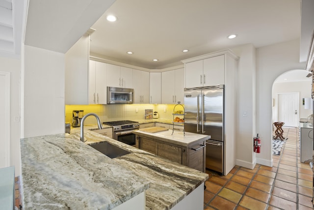 kitchen with sink, high end appliances, backsplash, white cabinetry, and light stone countertops