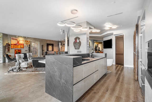 kitchen featuring light wood-type flooring, decorative light fixtures, a spacious island, and dark stone countertops