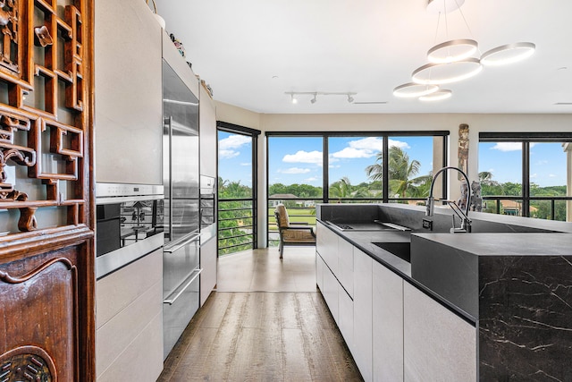 kitchen featuring decorative light fixtures, white cabinetry, sink, and hardwood / wood-style flooring