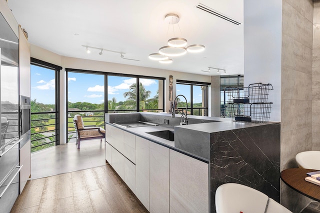 kitchen with plenty of natural light, white cabinetry, hanging light fixtures, and dark wood-type flooring