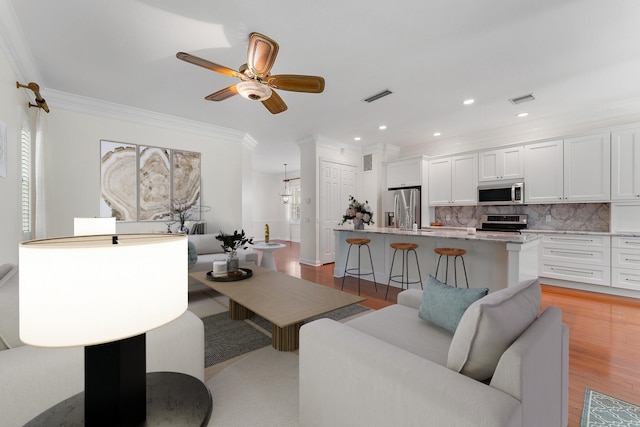 living room featuring ornamental molding, light wood-type flooring, and ceiling fan