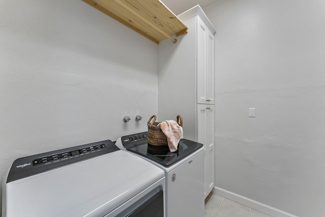 clothes washing area featuring separate washer and dryer, light tile patterned flooring, and cabinets