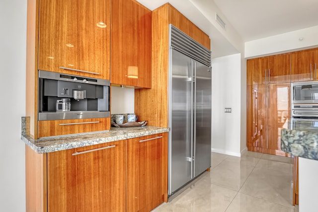 kitchen with light stone countertops, light tile patterned flooring, and built in appliances