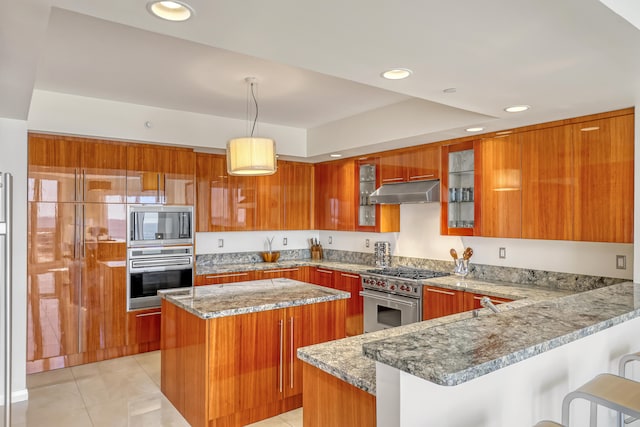 kitchen featuring light tile patterned floors, appliances with stainless steel finishes, a center island, light stone countertops, and a kitchen bar