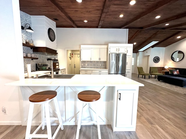 kitchen with light wood-type flooring, a breakfast bar, white cabinets, kitchen peninsula, and appliances with stainless steel finishes