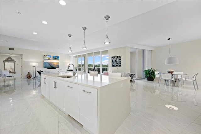 kitchen with decorative light fixtures, a kitchen island with sink, sink, and white cabinets