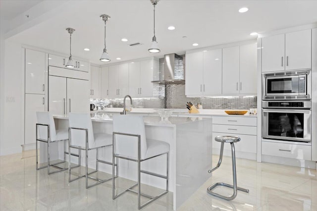 kitchen featuring white cabinets, hanging light fixtures, tasteful backsplash, wall chimney range hood, and built in appliances