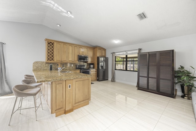 kitchen with appliances with stainless steel finishes, light stone countertops, sink, vaulted ceiling, and kitchen peninsula