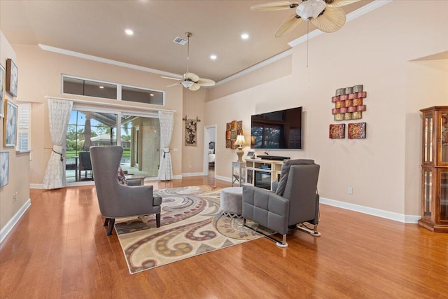 living room with a high ceiling, light hardwood / wood-style floors, ceiling fan, and crown molding