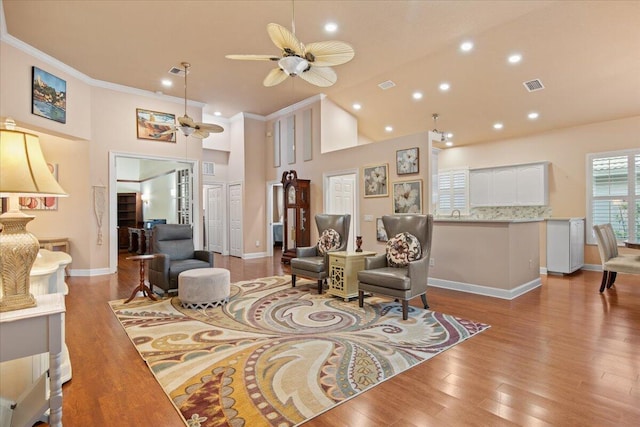 living room with a high ceiling, crown molding, light hardwood / wood-style floors, and ceiling fan