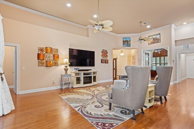 living room with light wood-type flooring, ceiling fan, a high ceiling, and crown molding