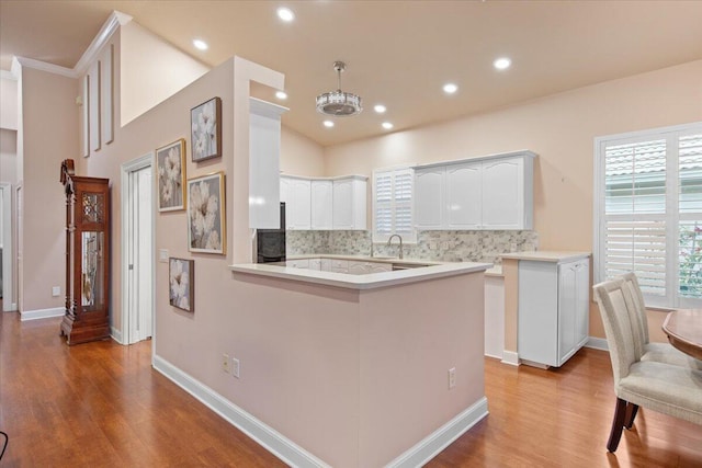 kitchen featuring decorative backsplash, white cabinetry, kitchen peninsula, pendant lighting, and light hardwood / wood-style flooring